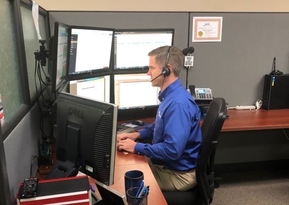Matt working at his desk with seven screens on a headset with a customer.